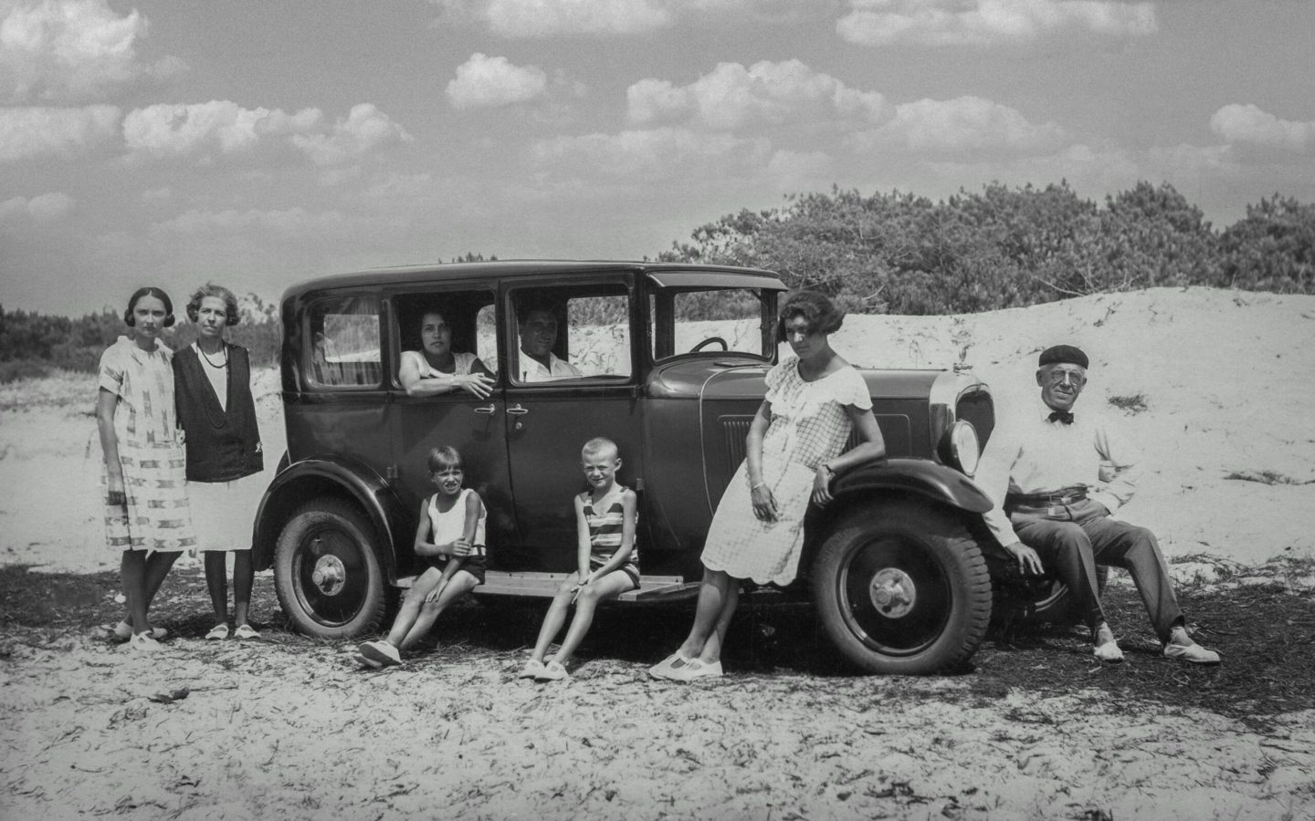 pexels-photo-28844203-28844203-1 A black and white vintage photograph of a family posing with a classic car outdoors, exuding a nostalgic feel.